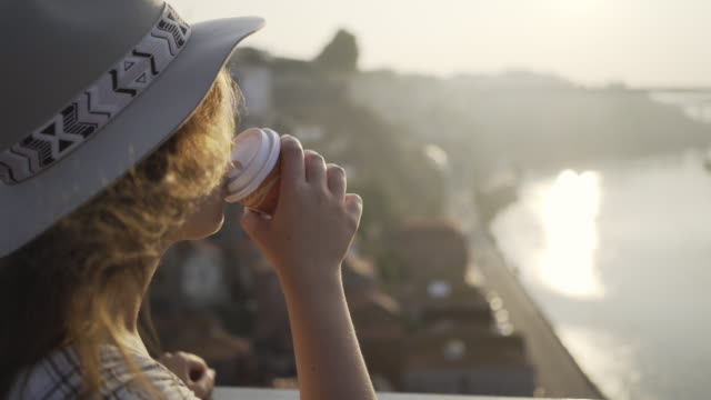 Lady-in-hat-drinking-from-cup-standing-on-bridge