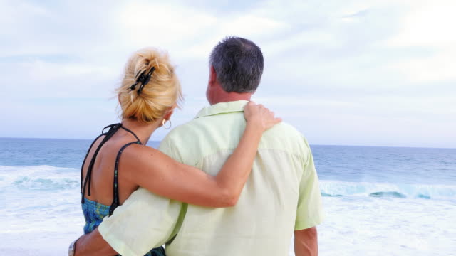 Close-up-of-an-older-couple-at-the-beach-with-their-arms-around-each-other-and-being-affectionate