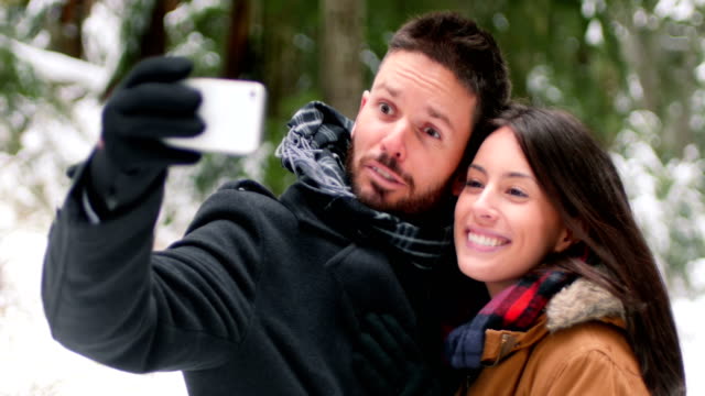 Couple-talking-and-taking-a-selfie-with-mobile-phone-on-a-winter-day