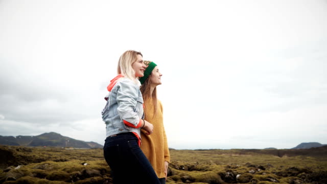 Hembra-de-dos-turistas-de-pie-en-el-campo-de-lava-en-Islandia-y-señalando-con-el-dedo-en-algo.-Feliz-mujer-hablando
