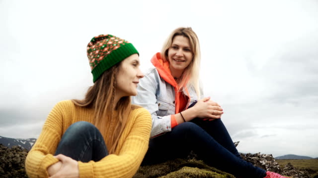 Zwei-glückliche-Frau-sitzt-auf-dem-Lavafeld-bedeckt-Moos-in-Island-und-im-Gespräch.-Touristen-Freunde-nach-einer-Wanderung-ausruhen