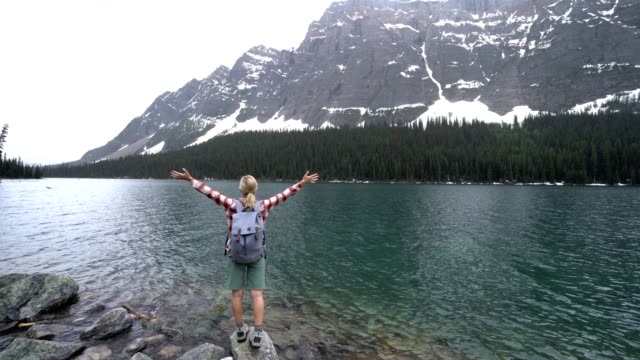Young-woman-arms-outstretched-by-mountain-lake