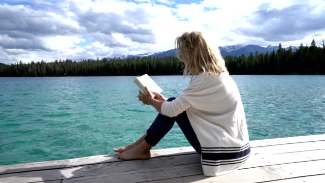 Mujer-joven-relajante-en-el-muelle-del-lago-con-el-libro,-Canadá