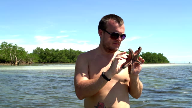 A-man-stands-at-sea-and-looks-at-a-starfish