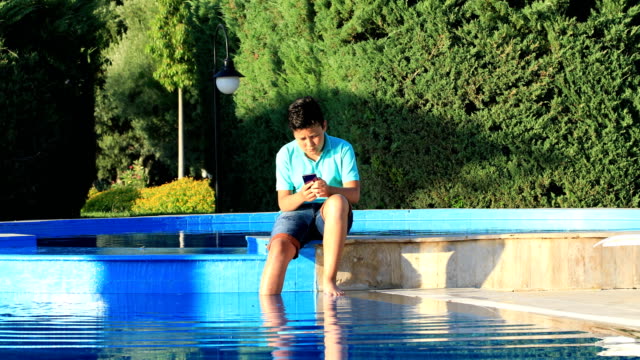 Young-boy-using-smartphone-near-the-pool