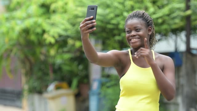 Young-happy-African-woman-using-phone-outdoors