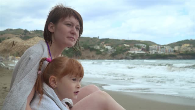 Mutter-und-Tochter-am-Strand-sitzen-und-schauen-auf-das-Meer