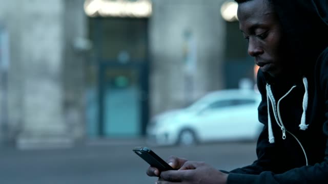 Negro-africano-joven-sentado-en-la-calle-escribiendo-en-smartphone