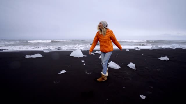 Mujer-de-turismo-joven-caminando-en-la-playa-de-arena-negra-en-la-playa-de-Jokulsarlon-Diamond