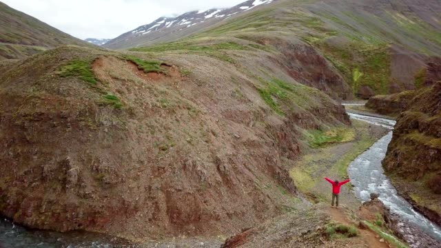 Stunning-drone-view-of-man-standing-arms-outstretched-on-top-of-canyon-in-Iceland