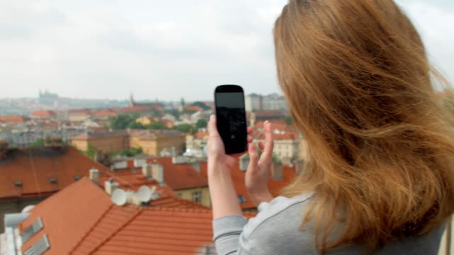 young-blonde-woman-is-taking-photos-of-panorama-of-Prague-city-by-modern-smartphone-in-daytime