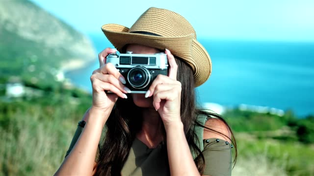 European-woman-in-hat-taking-photo-using-professional-camera-in-background-amazing-seascape