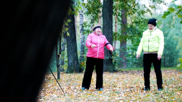 Mujer-madura-en-chaquetas-haciendo-gimnasia-en-un-parque-de-otoño-después-de-una-caminata-escandinava