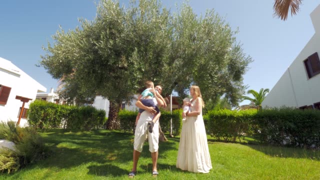 Parents-with-children-near-olive-tree-in-green-garden