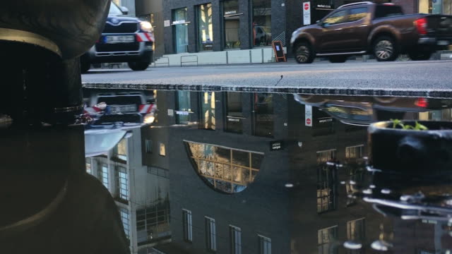 Großen-Bürgersteig-Regen-Pfütze-spiegelt,-Verkehr-und-Gebäude
