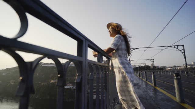 Lady-in-hat-and-dress-standing-on-bridge-and-looking-at-sunrise