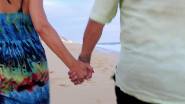 Close-up-of-an-older-couple-holding-hands-and-walking-down-the-beach