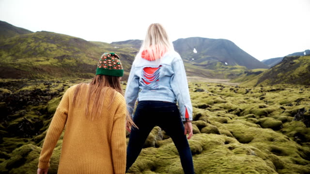 Two-tourists-woman-walking-through-the-lava-field-in-Iceland-covered-moss.-Girls-raises-hands,-feels-happy-and-freedom