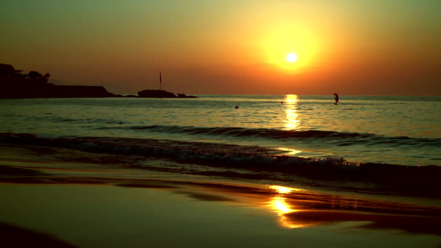 Silhouette-of-a-surfer,-swims-across-the-path-from-the-sun-to-the-sea-at-sunset.