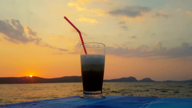 Kaffee-mit-einem-Strohhalm-gegen-den-Sonnenuntergang-und-das-Meer-eingefroren.