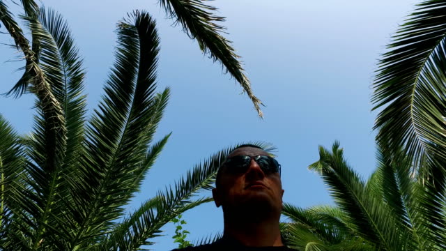Male-with-glasses-moving-under-Palm-Trees-tropical,-forest.-4k-steadicam-shot