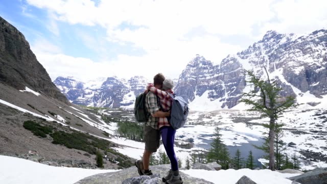 Junges-Paar-in-den-kanadischen-Rockies-Wandern-erreichen-Berggipfel-und-feiern-mit-einer-Umarmung