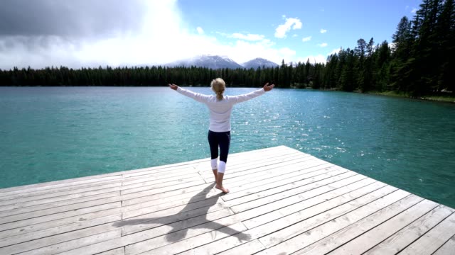Young-woman-arms-outstretched-on-lake-pier,-Canada