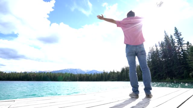 Hombre-joven-de-brazos-extendidos-en-el-muelle-del-lago,-Canadá