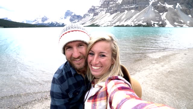 Couple-travelling-in-Canada-taking-selfies-by-stunning-mountain-lake-scenery