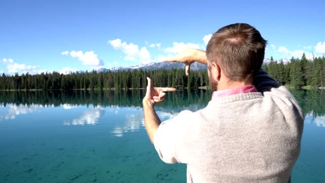 Hombre-está-parado-en-el-muelle-de-madera-sobre-el-impresionante-lago-y-hace-un-marco-con-las-manos