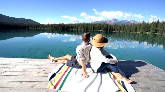 Junges-Paar-sitzt-auf-Holzsteg-über-dem-herrlichen-Bergsee-bewundern-Natur