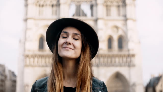 Portrait-of-young-beautiful-woman-in-hat-near-the-Notre-Dame-in-Paris,-France.-Female-looking-at-camera-and-smiling