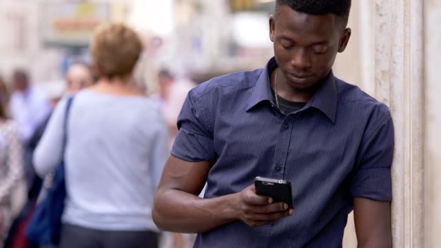 junge-attraktive-afrikanische-Mann-auf-der-Straße-konzentrierte-sich-auf-das-Schreiben-auf-smartphone