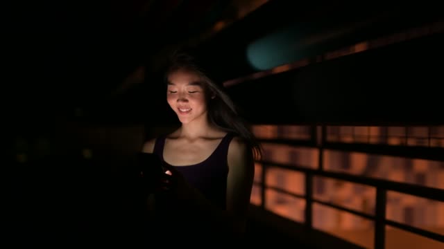 Schöne-asiatische-Frau-draußen-in-der-Nacht-mit-Handy