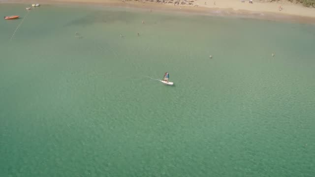Aerial-view-of-man-windsurfing-on-a-beach-with-people-swimming-in-Greece.