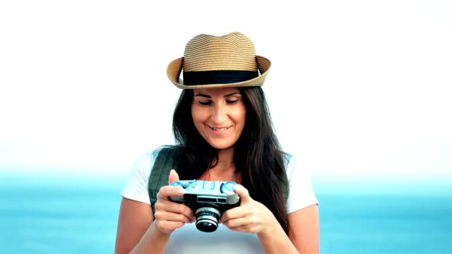 Portrait-of-beautiful-smiling-young-female-traveler-in-hat-taking-photo-using-retro-camera