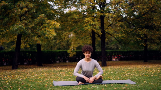 Flexible-junge-Dame-sitzt-auf-Matten-in-Yoga-Pose,-die-frische-Luft,-Ruhe-und-Entspannung-zu-genießen.-Gesunder-Lebensstil-für-urbane-Menschen,-aktive-Jugend-und-Natur-Konzept.