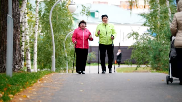 Las-mujeres-de-edad-caminando-por-la-acera-en-un-parque-de-otoño-durante-un-escandinavo