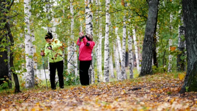 Reife-Frauen-wirft-Blätter-auf-einander-bei-einem-skandinavischen-Spaziergang