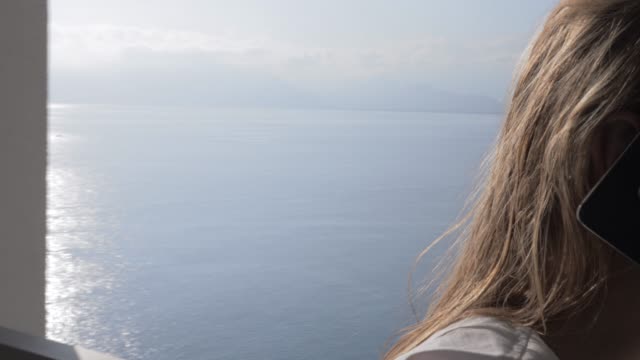 Emotionale-Frau-mit-Handy-auf-dem-Balkon-mit-Blick-aufs-Meer-zu-sprechen