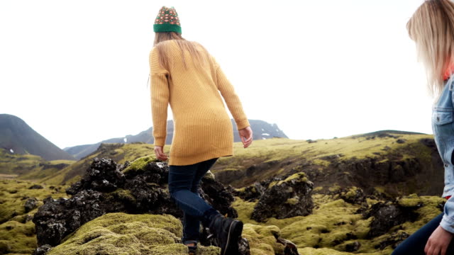 Freedom:-two-tourists-woman-raises-hands-on-the-lava-field-covered-moss-in-Iceland.-Friends-feeling-happy-after-hiking