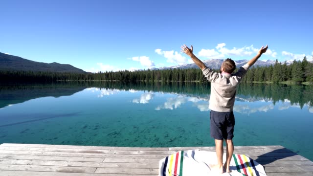Man-arms-outreached-by-alpine-lake-in-the-Canadians-rockies