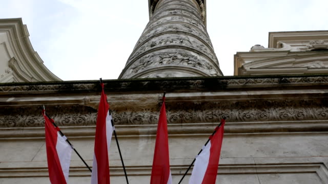 tracking-shot-from-Austrian-flags-towards-carved-column-of-Karlsplatz-church,-Vienna-Austria