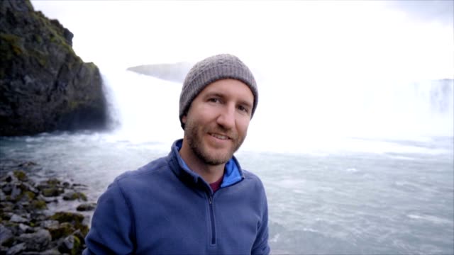 Porträt-des-jungen-Mannes-touristischen-Reisen-mit-herrlichen-Wasserfall-in-Island