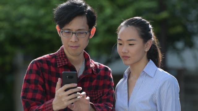 Junge-asiatische-Paar-mit-Handy-zusammen-im-freien
