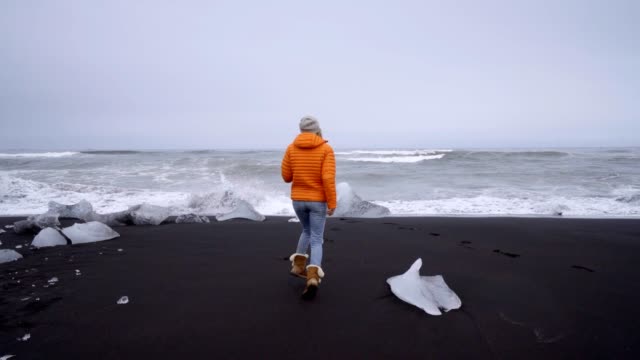 Mujer-de-turismo-joven-caminando-en-la-playa-de-arena-negra-en-la-playa-de-Jokulsarlon-Diamond
