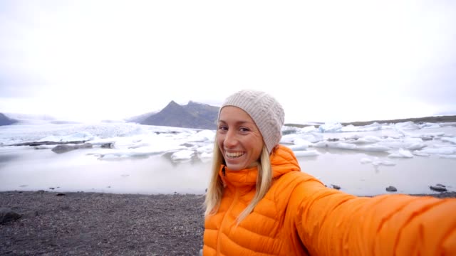 Slow-motion-Young-woman-taking-selfie-with-glacier-lake,-icebergs-floating-on-water