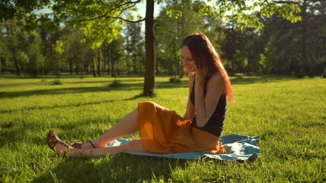 Mujer-sentarse-sobre-la-hierba-verde-y-tener-conversación-via-selfphone