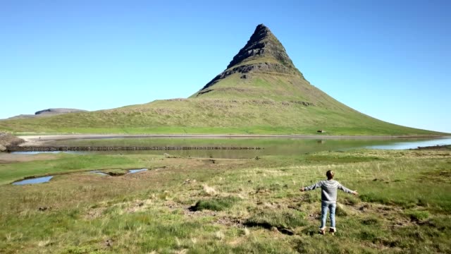 Drone-aerial-view-of-Caucasian-female-arms-raised-for-positive-emotions,-Kirkjufell-mountain-on-background.-Shot-in-West-Iceland,-Springtime.-People-travel-carefree-lifestyles-concept--4K