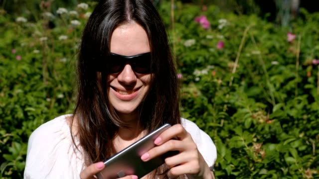 Woman-is-playing-a-game-on-mobile-phone-sitting-in-park-in-sunny-day.